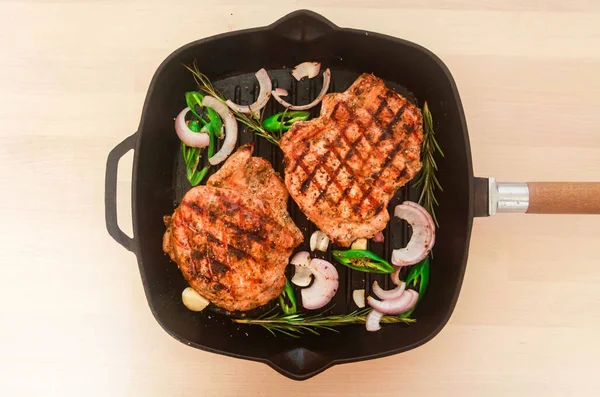 Stekt Fläskstek i en stekpanna med varm grön paprika och lök på en mörk bakgrund. — Stockfoto