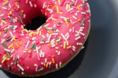 Pembe donut, mavi bir tabakta renkli şekerlemeler.