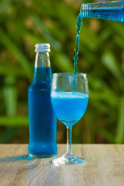glass and a bottle with a blue drink stand on a table on a green background