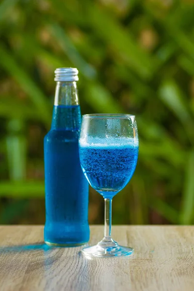 glass and a bottle with a blue drink stand on a table on a green background