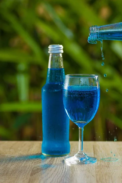 glass and a bottle with a blue drink stand on a table on a green background