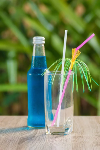 glass and a bottle with a blue drink stand on a table on a green background