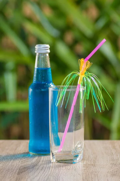 glass and a bottle with a blue drink stand on a table on a green background