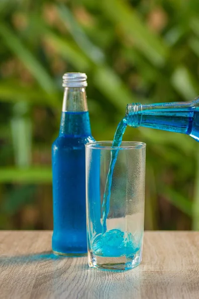 glass and a bottle with a blue drink stand on a table on a green background