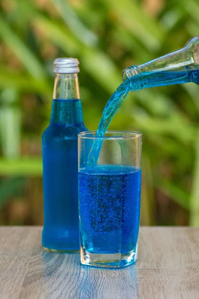 glass and a bottle with a blue drink stand on a table on a green background