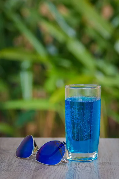 glass with a blue drink stand on a table on a green background