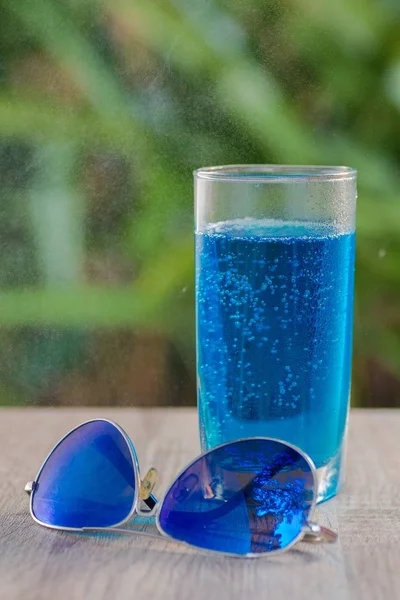 glass with a blue drink stand on a table on a green background
