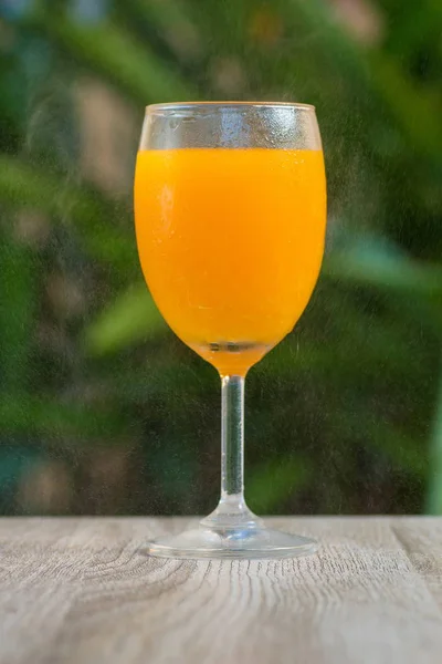 glass with orange drink stand on a table on a green background