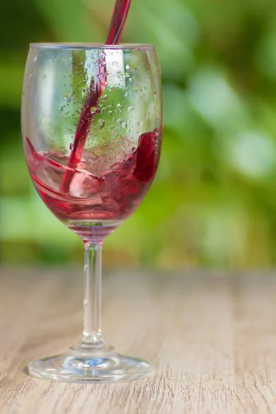 Transparent misted glass with grape juice or wine on a background of green bushes in different lighting