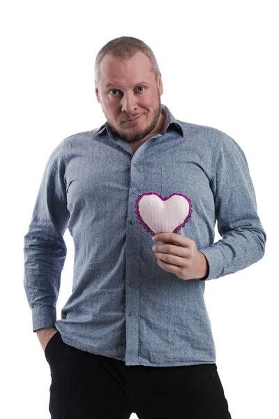 emotional actor man in a gray shirt with a soft toy heart in hands on a white background in studio