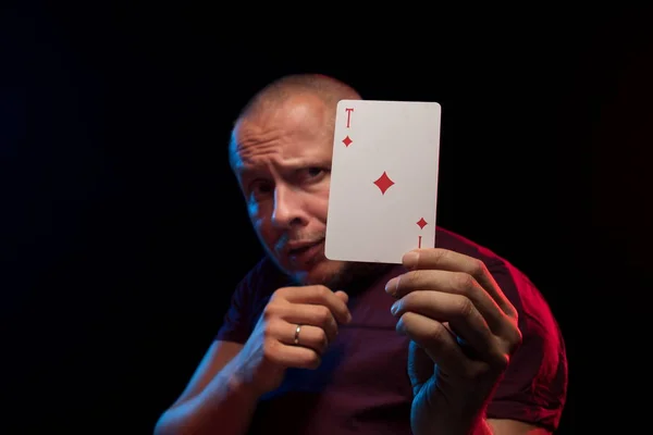 man holds a deck of cards and shows tricks in a scenic light