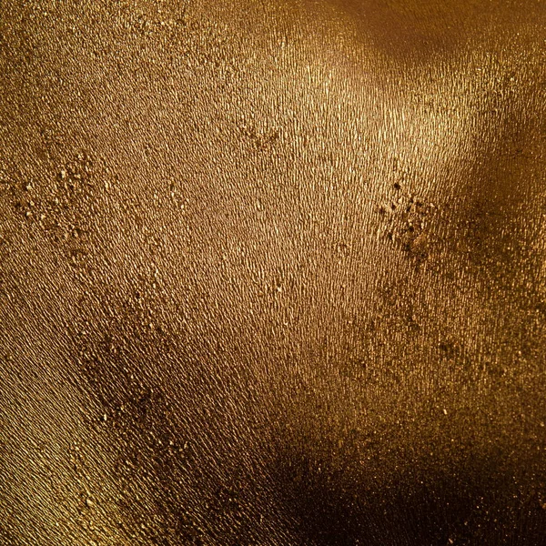 Male athlete bodybuilder in gold body paint posing on black background