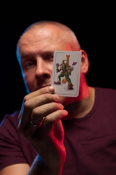 man holds a deck of cards and shows tricks in a scenic light