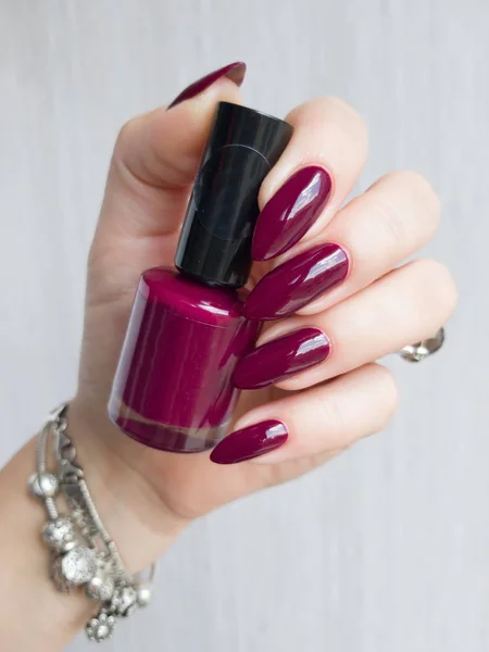 Female hand with long nails holds a bottle with a bright nail polish