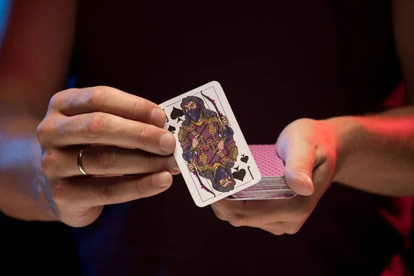 man holds a deck of cards and shows tricks in a scenic light.