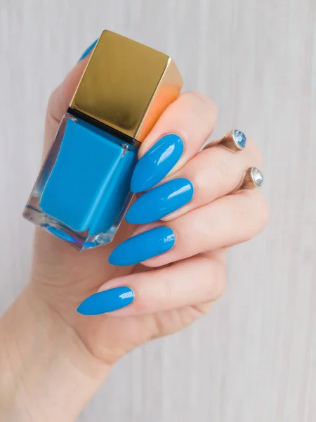 Female hand with long nails holds a bottle with a bright nail polish