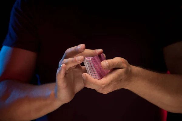 man holds a deck of cards and shows tricks in a scenic light.