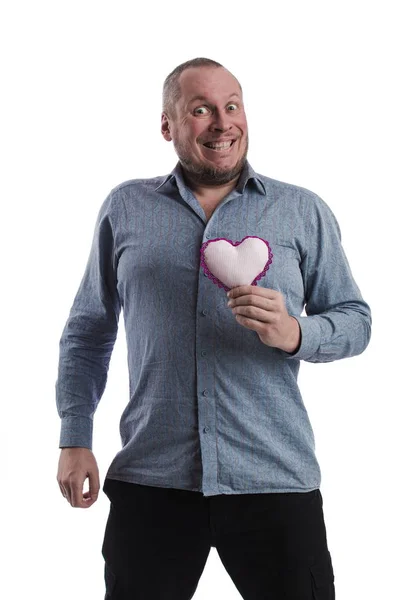 emotional actor man in a gray shirt with a soft toy heart in hands on a white background in studio