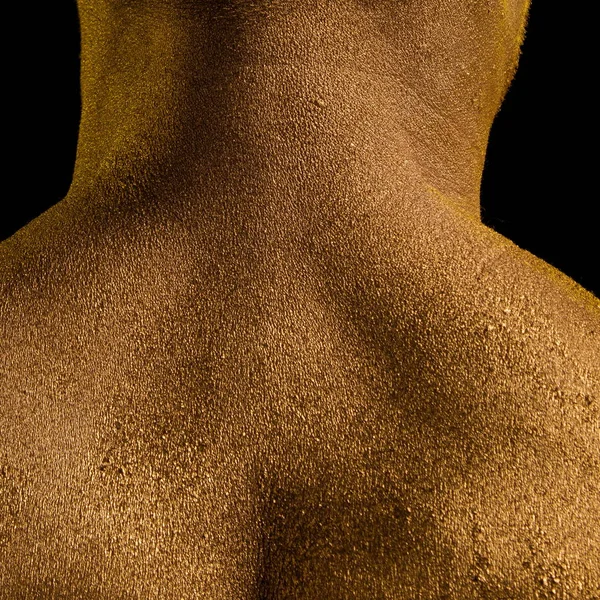 Male athlete bodybuilder in gold body paint posing on black background