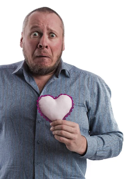 emotional actor man in a gray shirt with a soft toy heart in hands on a white background in studio