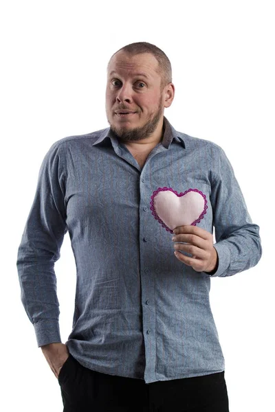 emotional actor man in a gray shirt with a soft toy heart in hands on a white background in studio