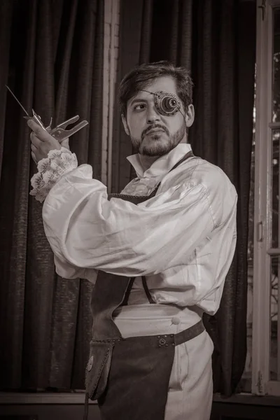 young man dressed in clothes in the style of steampunk, posing in the interior against the background of large windows