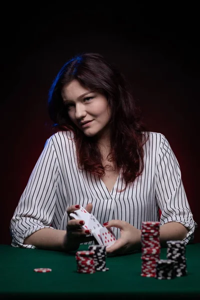 Brunette actress girl plays cards over green cloth posing on a dark background in blue and red light