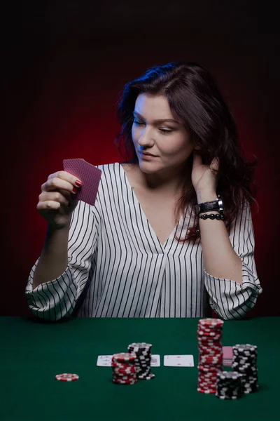 Brunette actress girl plays cards over green cloth posing on a dark background in blue and red light