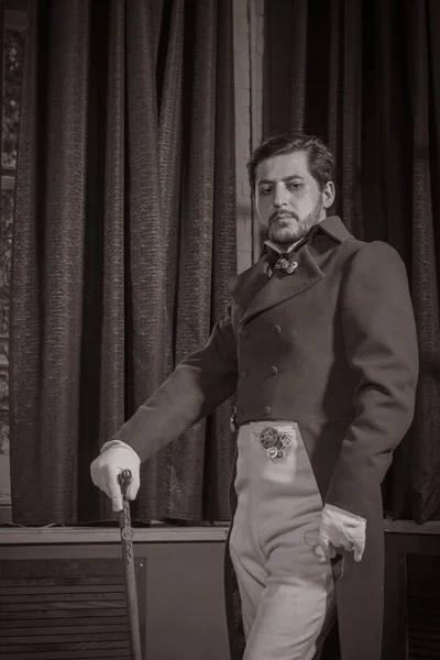 young man dressed in clothes in the style of steampunk, posing in the interior against the background of large windows