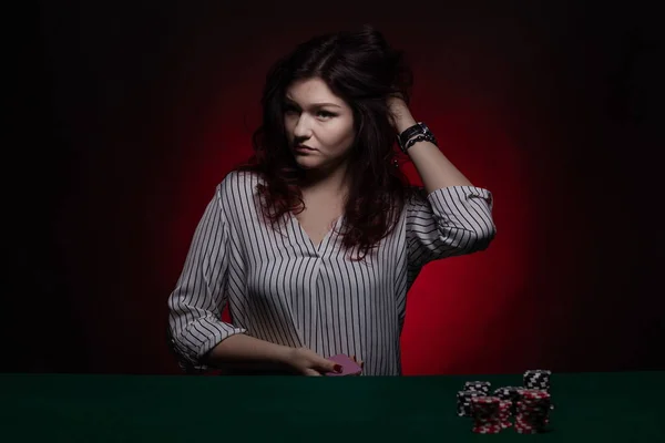 Brunette actress girl plays cards over green cloth posing on a dark background in blue and red light