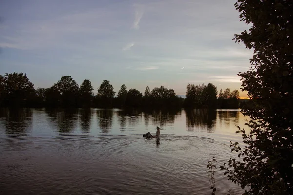 Blonde girl in white and red bodypain jumps  with a horse in the lake at sunset