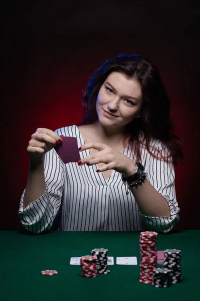 Brunette actress girl plays cards over green cloth posing on a dark background in blue and red light