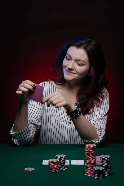 Brunette actress girl plays cards over green cloth posing on a dark background in blue and red light