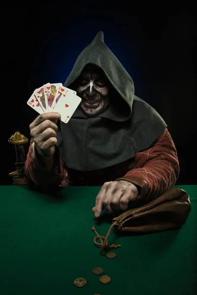 male actor in the costume of a medieval inquisitor playing poker at a card table with a green cloth