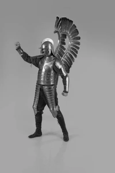 Man in armor of hussar legion posing on gray background, black and white photo