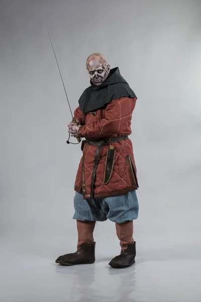 Male actor in zombie viking make up and costume posing with weapon on grey background