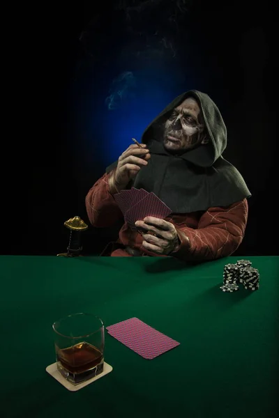 male actor in the costume of a medieval inquisitor playing poker at a card table with a green cloth