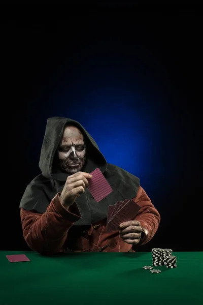 male actor in the costume of a medieval inquisitor playing poker at a card table with a green cloth