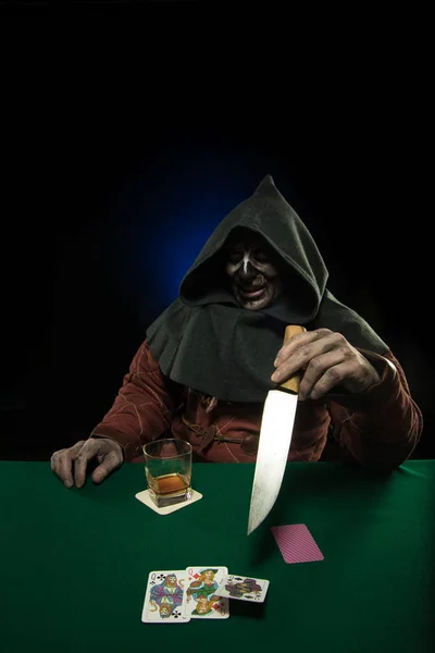 male actor in the costume of a medieval inquisitor playing poker at a card table with a green cloth