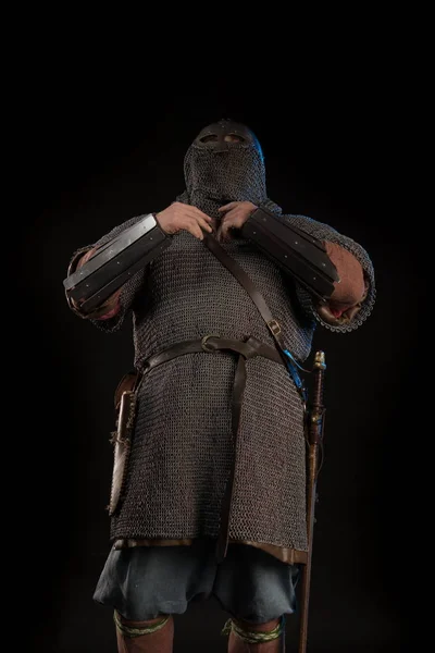 Portrait of a brutal Viking in a military mail with a helmet on his head posing on a black background. Early medieval period