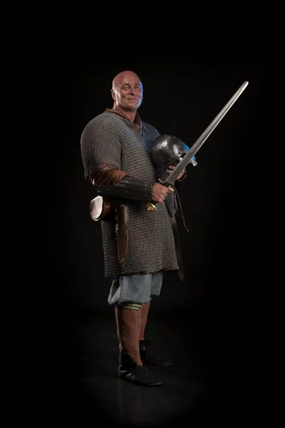 Portrait of a brutal bald man viking in linen clothes  posing against a black background. Early medieval period