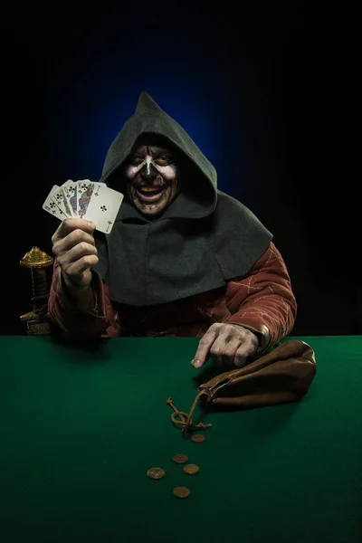 male actor in the costume of a medieval inquisitor playing poker at a card table with a green cloth