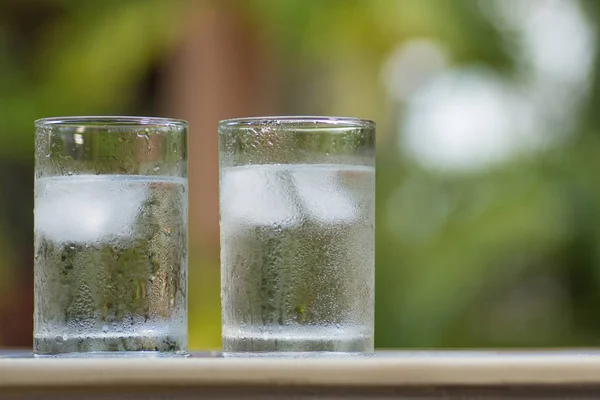 Transparent misted glasses with water and ice on table outdoors