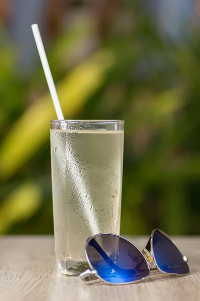 Transparent misted glass with water and straw on table with sunglasses