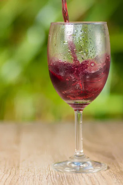 Transparent misted glass with grape juice or wine on background of green bushes