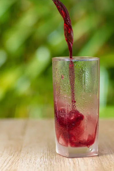 Transparent misted glass with grape juice or wine on background of green bushes