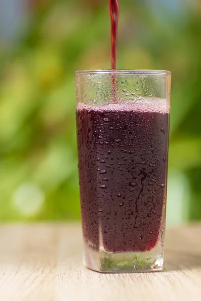 Transparent misted glass with grape juice or wine on background of green bushes