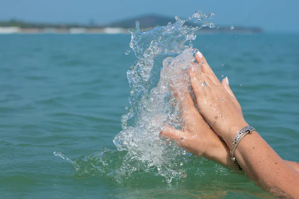 Female hands with white nail polish in the turquoise sea water on the background of the beach