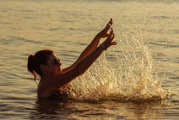 Brunette woman in  sunglasses in blue sea poses for photo at sunset