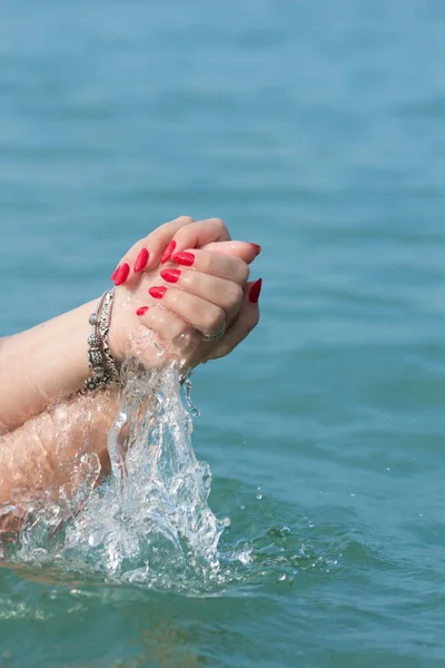 Female hands with white nail polish in the turquoise sea water on the background of the beach